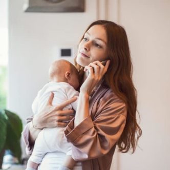Eine junge Mutter informiert sich am Handy über Minijobs in Elternzeit