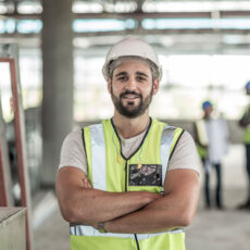 Ein Bauarbeiter steht auf der Baustelle und lächelt in die Kamera