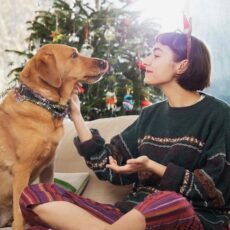 Eine junge Frau sitzt mit einem Hund vorm Weihnachtsbaum.
