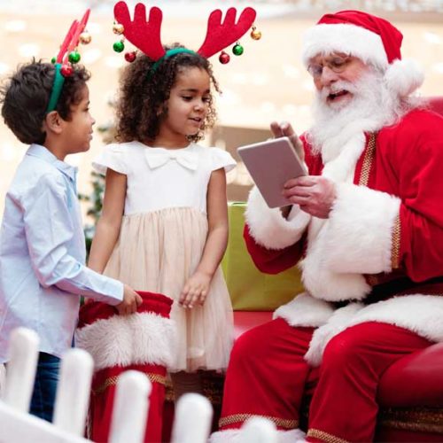 Ein Mann als Weihnachtsmann verkleidet spricht mit zwei Kindern über ihre Wünsche.