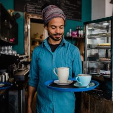 Ein junger Mann trägt ein Tablett mit Kaffee.