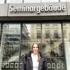 Eine junge Frau steht vor einem Gebäude und lächelt.