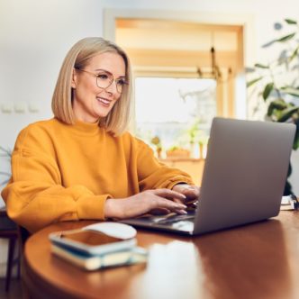 Eine Frau sitzt zu Hause an einem Tisch und arbeitet am Laptop