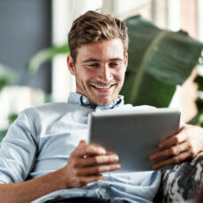 Aufnahme eines glücklichen jungen Mannes, der sein Tablet benutzt, während er der Couch entspannt