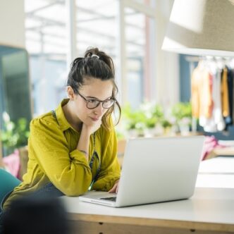 Junge Frau mit Brille arbeitet konzentriert an einem Laptop in einem hellen, modernen Raum.