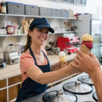 Eisverkäuferin in Eisdiele reicht lächelnd zwei Eiswaffeln über die Theke.