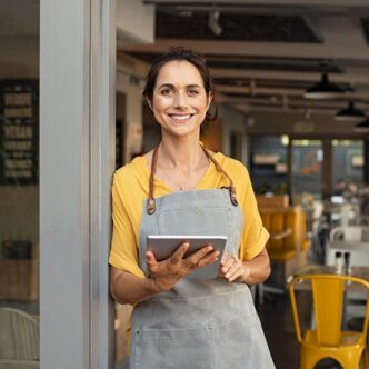 Alt-Texte für Magazin-Bilder sagte: „Eine Frau in einer grauen Schürze hält ein Tablet und lächelt vor einem Café-Hintergrund.“
