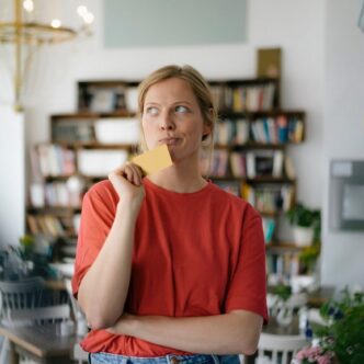 Eine junge Frau in einem roten T-Shirt hält nachdenklich einen Zettel.