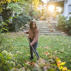 Eine junge Frau harkt Laub im Garten.