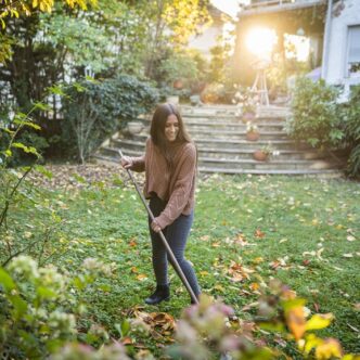 Eine junge Frau harkt Laub im Garten.